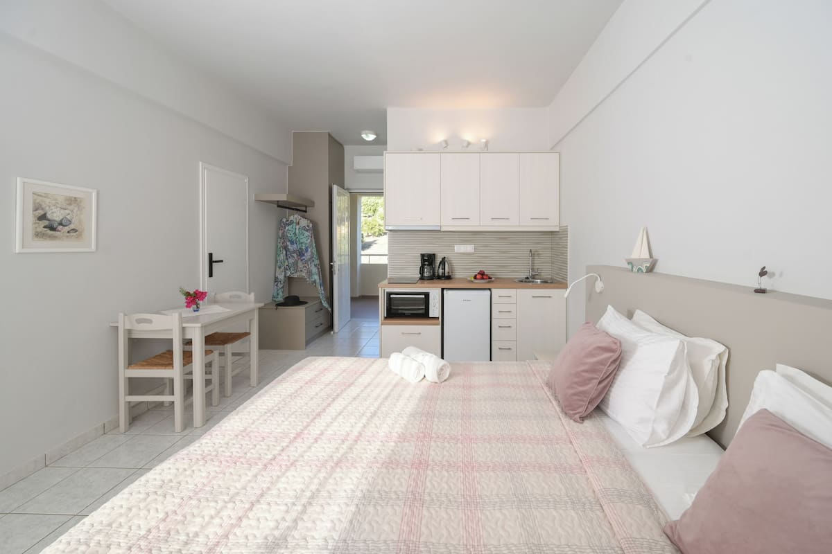 A bedroom with a bed, bedside table, and a view of the kitchen.