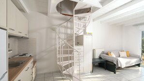 Una cocina moderna con armarios blancos, estufa integrada y una escalera espiral blanca que sube a un nivel superior.