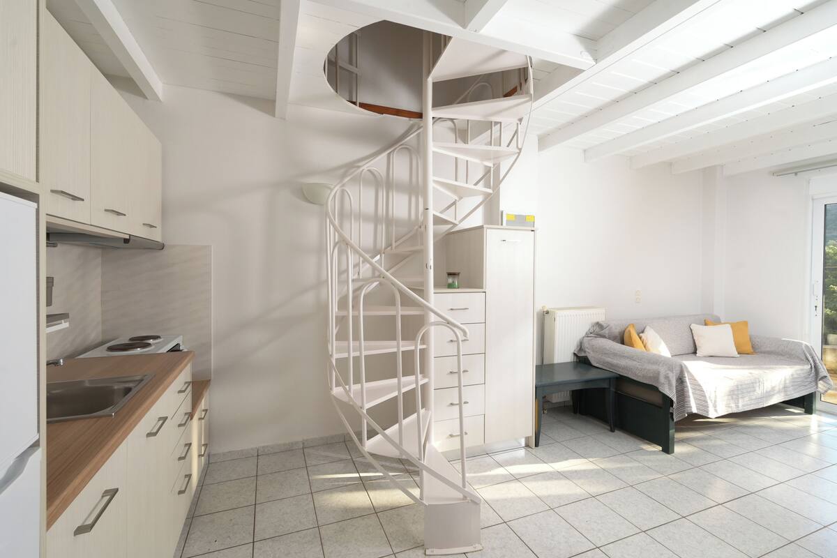 A modern kitchen with white cabinets, a built-in stove, and a white spiral staircase leading to an upper level.