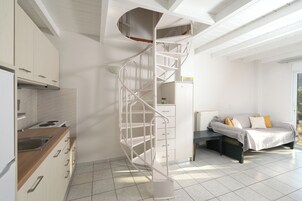 Una cocina moderna con armarios blancos, estufa integrada y una escalera espiral blanca que sube a un nivel superior.