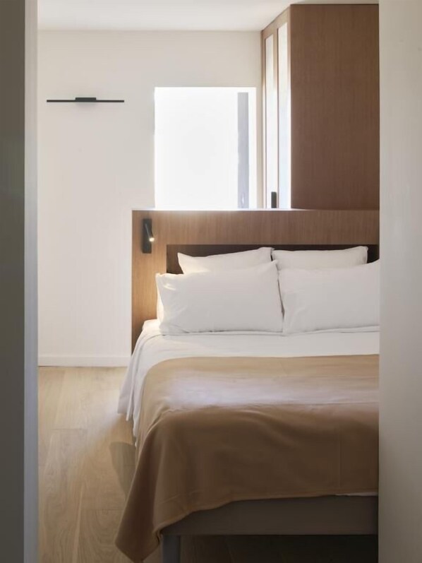 A modern bedroom with a wooden headboard, a large window, and a minimalist design.