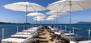 A row of sun loungers with white umbrellas on a boat deck, facing a calm sea.