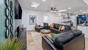 Una sala de estar moderna con un sofá modular, una mesa de centro y una chimenea. Se observa un área de cocina al fondo.