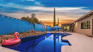 Una piscina con un flotador de flamenco rosa, un muro de piedra y vistas al atardecer.