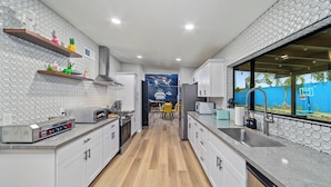 Una cocina moderna con armarios blancos, suelo de madera y pared azul con un mural.