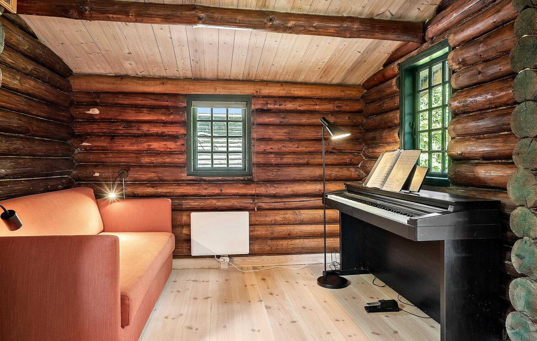 L’intérieur d’une cabane en rondins, avec un piano, un canapé et une fenêtre équipée de stores.