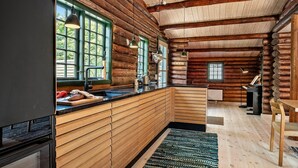 A log cabin interior with a kitchen area featuring wooden cabinetry, a black countertop, and a large window with green shutters. - Beautiful home in Præstø with WiFi (Præstø)