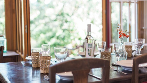A dining table set with glassware and a bottle of Gris, with a view of greenery through the window. - Appartement Gracieuse - Welkeys (Soorts-Hossegor)