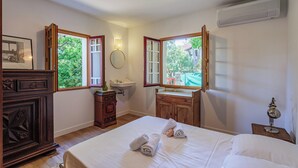 A bedroom with a large bed, wooden dresser, vanity with mirror, and a window with a view of greenery. - Appartement Gracieuse - Welkeys (Soorts-Hossegor)