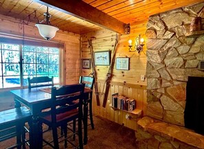 L’intérieur d’un chalet en bois comprend une table à manger, des chaises, une cheminée et des tableaux encadrés accrochés aux murs.