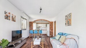 A living room with a TV, a glass coffee table, a sofa, and a kitchen in the background. - Appartement Delmas - Welkeys (Antibes)
