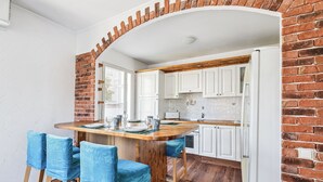 A kitchen with white cabinets, a wooden island with blue chairs, and a brick archway. - Appartement Delmas - Welkeys (Antibes)
