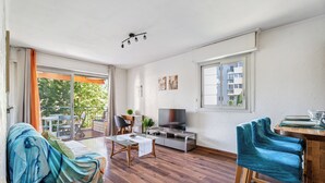 A modern living room with a sofa, TV, and a dining area with chairs and a table. - Appartement Delmas - Welkeys (Antibes)