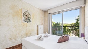 A bedroom with a large bed, a window with a view, and a wall-mounted artwork. - Appartement Delmas - Welkeys (Antibes)