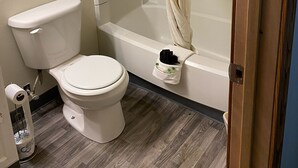 A bathroom with a toilet, bathtub, and shower curtain. - Homestead Inn Extended Stay - 3 nights minimum (Wolf Point)