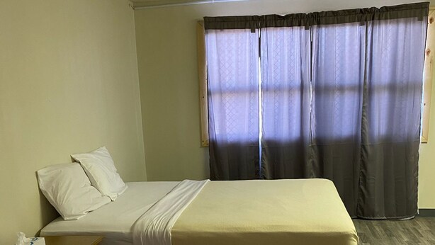 A hotel room with two beds, a bedside table with a remote control, and a window with curtains. - Homestead Inn Extended Stay - 3 nights minimum (Wolf Point)