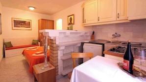 Une cuisine compacte avec des meubles blancs, une table à manger agrémentée d’une bouteille et d’un verre, et un banc avec des coussins orange.