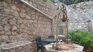 Un mur de pierre, une table en métal, une chaise et une structure en béton avec un récipient en métal.