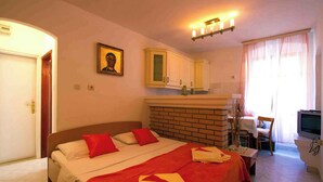 Une chambre d’hôtel comprenant un lit, une télévision, un bureau avec une chaise, une salle de bain et une fenêtre avec des rideaux.