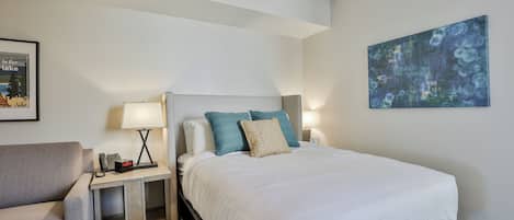 Une chambre d’hôtel avec un grand lit, deux tables de chevet avec des lampes, une chaise et un tableau encadré au mur.