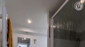 A bathroom with a glass shower enclosure, a towel rack with a yellow towel, a small window, and a door with a logo. - Maison Marmillons - Pavilion (AIX LES BAINS)