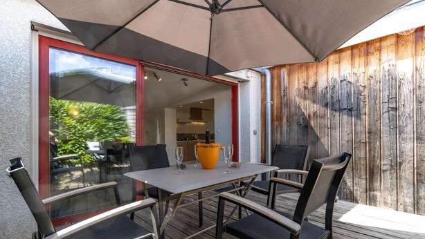An outdoor patio with a table and chairs, a large umbrella, and a wooden fence. - Maison Marmillons - Pavilion (AIX LES BAINS)