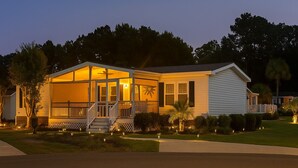 A single-story house with a covered porch, a small front yard, and a well-lit exterior at dusk. - Charming 3-bedroom house in Garden City, featuring two covered porches! (Murrells Inlet)