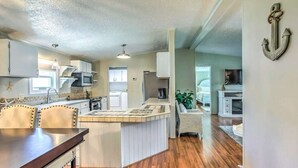 A compact kitchen with white cabinets, a central island, and a dining area with a wooden table. - Charming 3-bedroom house in Garden City, featuring two covered porches! (Murrells Inlet)