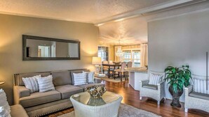 A living room with a sofa, a coffee table, and a dining area with chairs and a chandelier. - Charming 3-bedroom house in Garden City, featuring two covered porches! (Murrells Inlet)