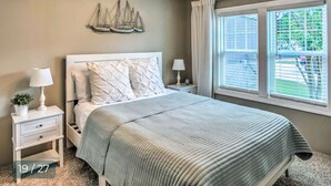 A bedroom with a bed, nightstands, a window with curtains, and a decorative wall piece. - Charming 3-bedroom house in Garden City, featuring two covered porches! (Murrells Inlet)