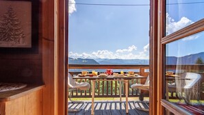 A wooden deck with a table set for breakfast, overlooking a mountainous landscape.
