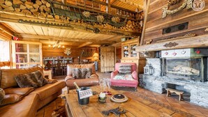 A cozy log cabin interior with a fireplace, leather sofas, and a dining area.