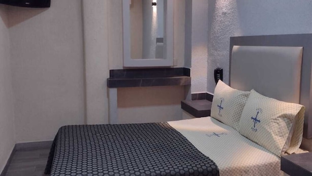 A bedroom with a bed, a TV mounted on the wall, a mirror, and a bedside table. - Hotel Astur (Guadalajara)