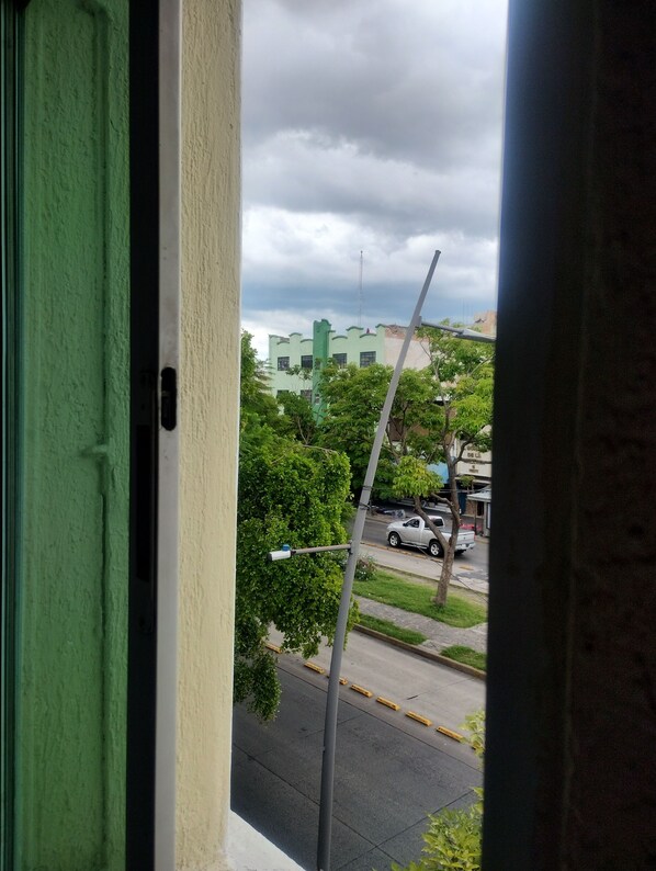 Vista a través de una ventana con una puerta verde, mostrando una calle con coches aparcados y edificios al fondo.