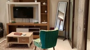 En stue med et fladskærms-tv, et tv-møbel i træ, en grøn lænestol, et sofabord og en skydedør med glas.