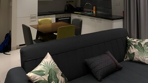 En moderne stue med en mørk sofa, et spisebord og et køkken i baggrunden.