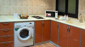A compact kitchen with a washing machine, microwave, and cabinets. - Dar Alslama Apartment (Jeddah)
