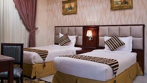 A hotel room with two beds, a nightstand, a chair, and a wall-mounted lamp. - Dar Alslama Apartment (Jeddah)
