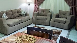 A living room with a sofa, two armchairs, a coffee table, and a lamp. - Dar Alslama Apartment (Jeddah)