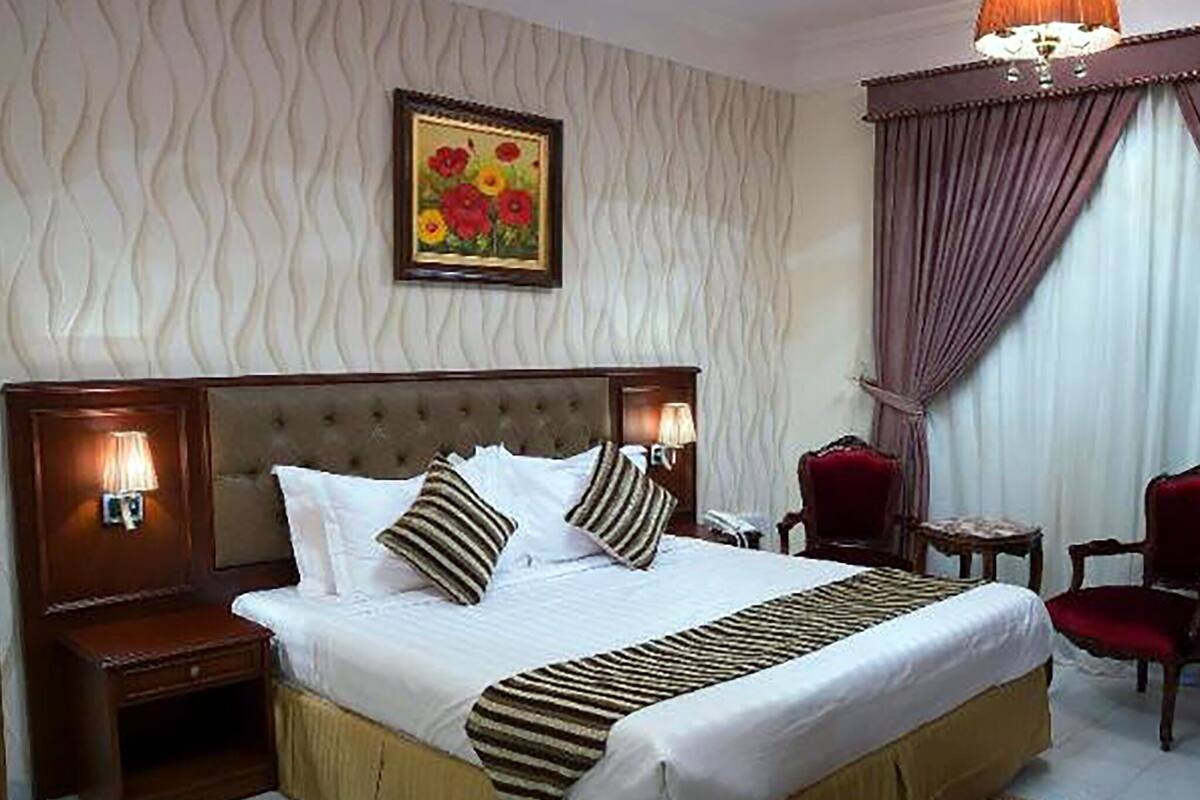 A hotel room with a large bed, a nightstand, a chair, and a painting on the wall.