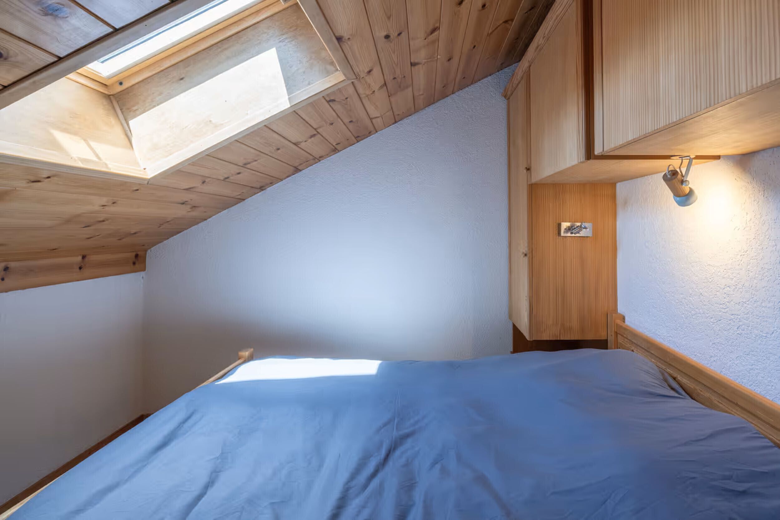 A small, cozy room with a sloped ceiling, a skylight, a bed, and wooden cabinets.