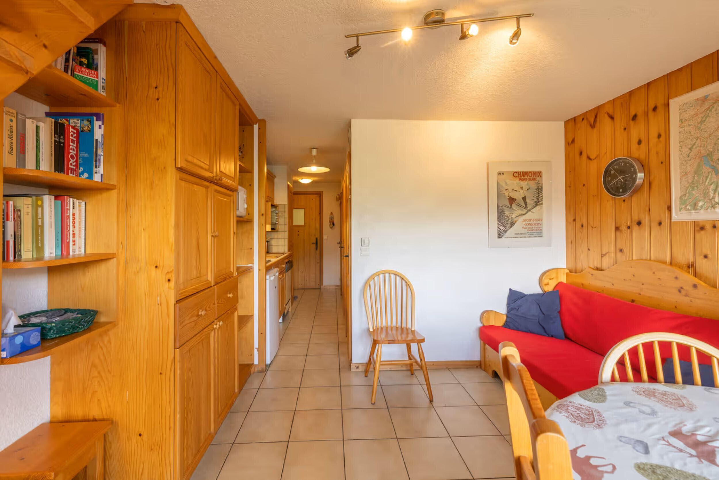 A cozy room with wooden furniture, a bookshelf, a dining table, and a red sofa.