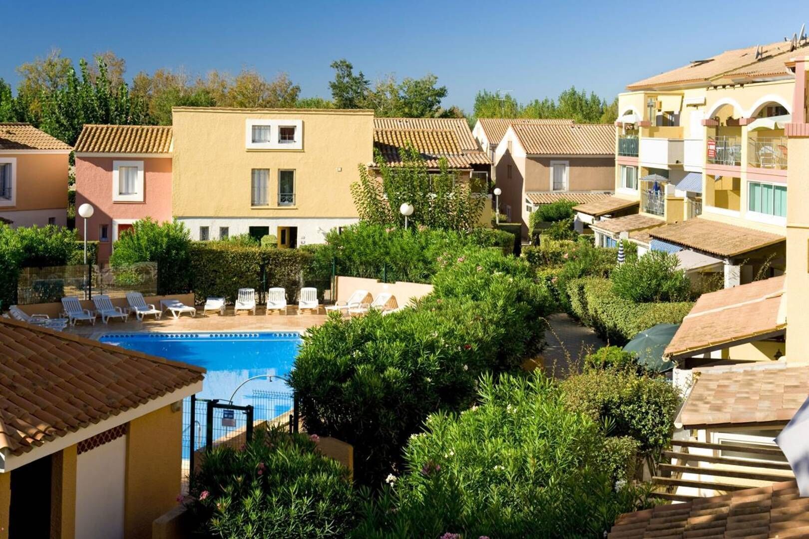 Un quartier résidentiel doté d’une piscine entourée de verdure et de plusieurs bâtiments aux toits recouverts de tuiles.
