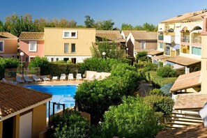 Zona residencial com piscina cercada por vegetação e vários edifícios com telhados em azulejo.