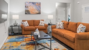 A living room with two orange sofas, a coffee table, and two side tables with lamps. There is a colorful rug on the floor and a painting on the wall. - NEW 3-BR townhome in delightful Spring Hill with WiFi, AC and many amenities (Spring Hill)