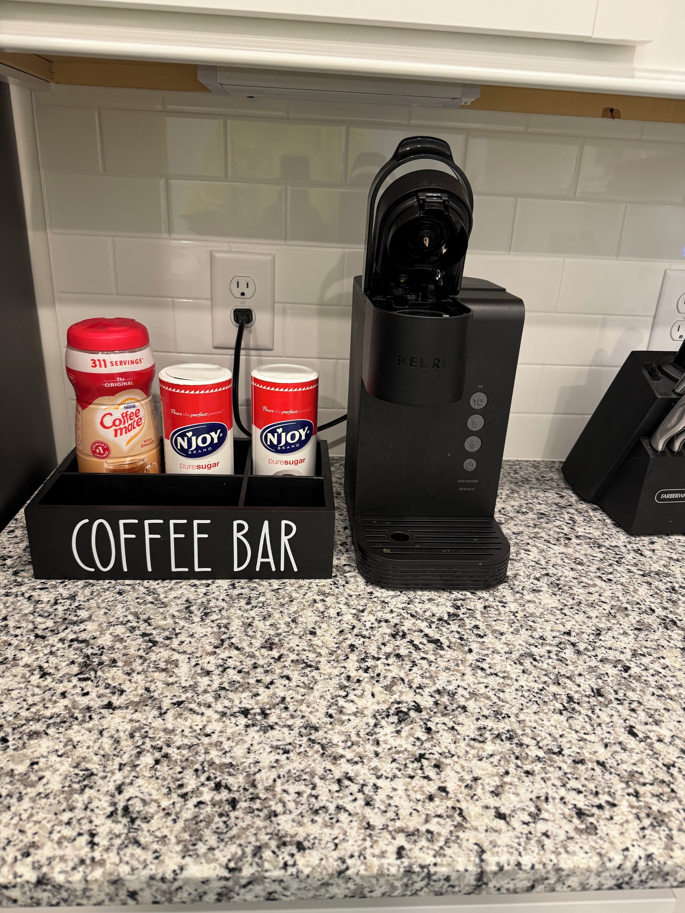 Un comptoir de cuisine avec une machine à café, une enseigne indiquant un bar à café et deux boîtes de café.