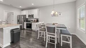 A modern kitchen with white cabinetry, stainless steel appliances, and a dining area with a table and chairs. - NEW 3-BR townhome in delightful Spring Hill with WiFi, AC and many amenities (Spring Hill)