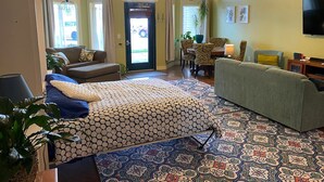 Ein geräumiges Wohnzimmer mit einem großen Bett, einer Couch und einem Essbereich. Ein Deckenventilator, ein Fernseher und eine Tür nach draußen sind ebenfalls vorhanden.