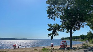 Blick auf einen See, bewölkter Himmel, eine rote Rettungsstation und Personen in der Nähe des Wassers.
