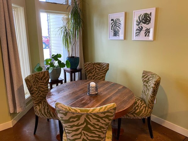A dining area with a round wooden table surrounded by zebra-patterned chairs, a potted plant, and framed artwork on the wall.